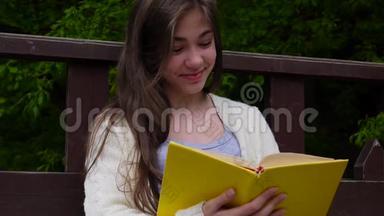 欢快的少女读书的肖像，春天坐在森林的长凳上，在户外学习。 高清视频